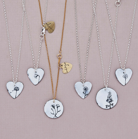 A collection of necklaces with heart-shaped pendants, some with floral patterns, displayed against a light pink background.